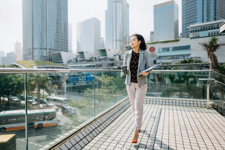 Woman standing on patio holding documents and coffee while overlooking a city skyline